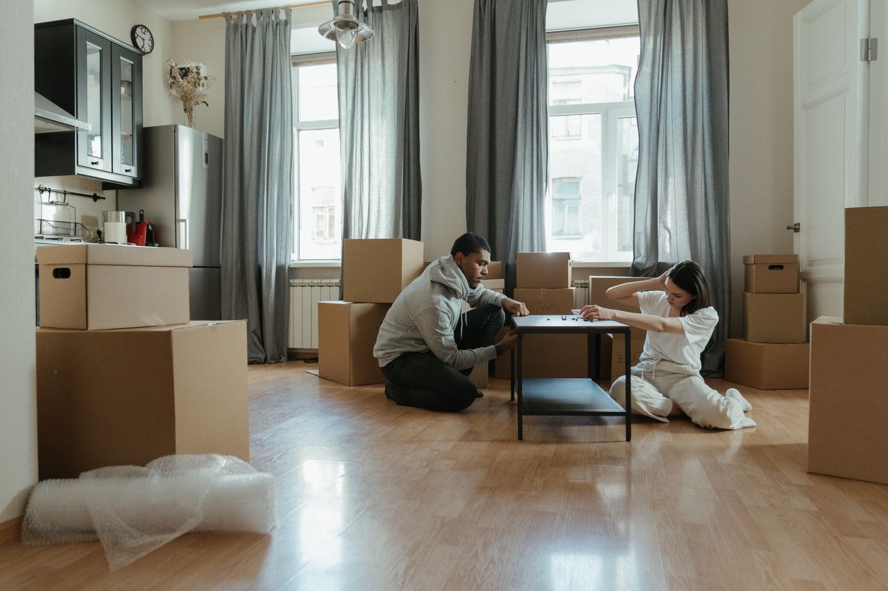 about-02 Young couple assembling furniture in their new apartment, surrounded by cardboard boxes.